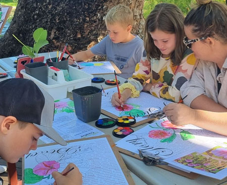 Children painting with watercolours at an outdoor table in Darwin's Botanic Gardens during Botanically Creative Workshops.