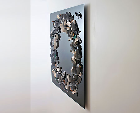 A side-on view of an artwork made up of ceramic leaves, curving lines, stylised fish, pebbles and gum nuts laid in a broad circle on a black glass background.