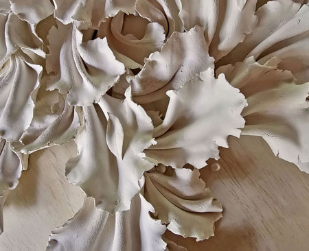 An artwork called 'Force of Nature' made up of over 80 folded ceramic pieces, ribbons, and leaves, arranged in an outward flow on plywood.