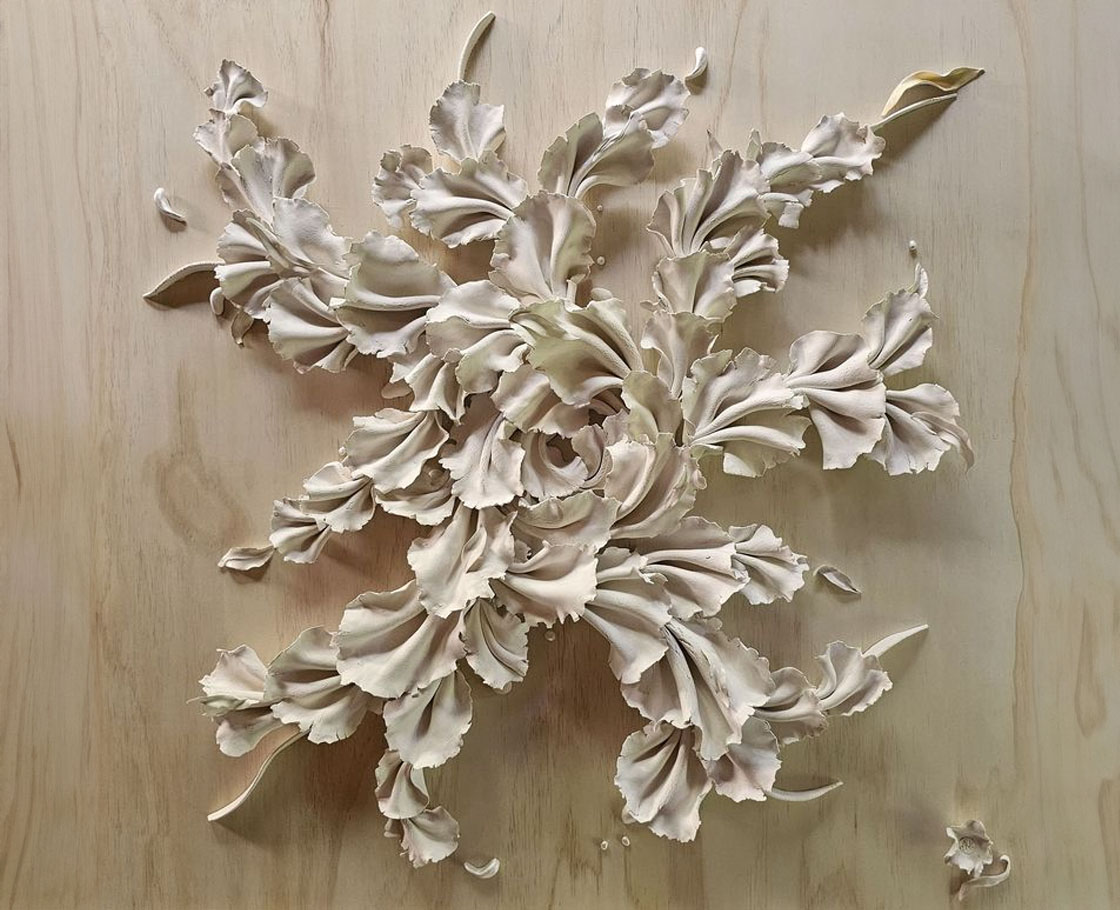 An artwork called 'Force of Nature' made up of over 80 folded ceramic pieces, ribbons, and leaves, arranged in an outward flow on plywood.