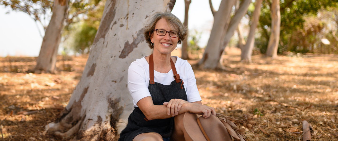 Artist Maria Kraatz sitting in the shade of eucalyptus trees in a park.